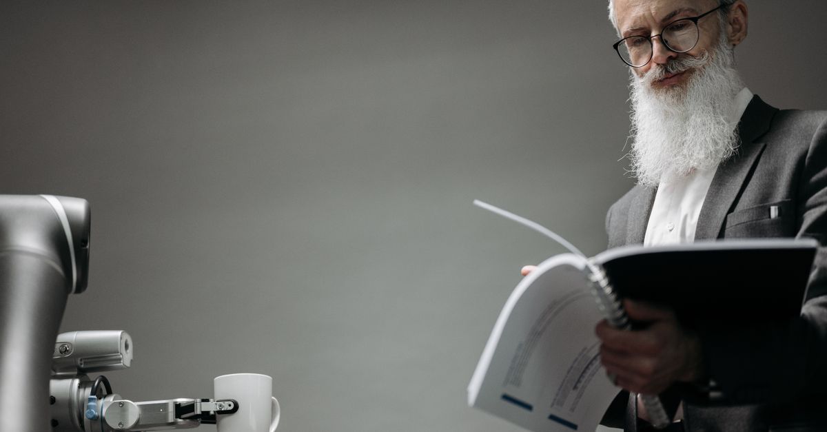 Elderly man reads as a robotic arm holds a coffee cup, showcasing technology integration.