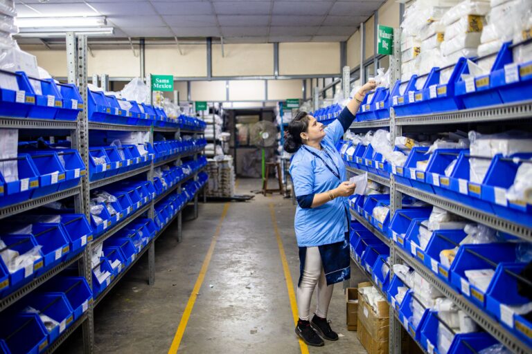 Woman in uniform organizing inventory in a warehouse aisle with labeled bins