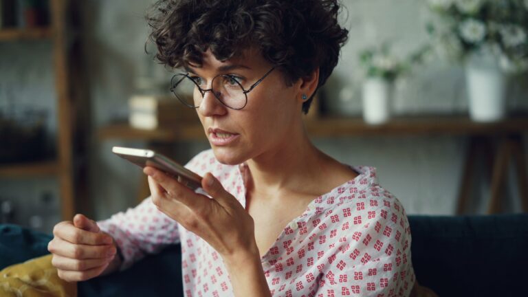 Casual woman using AI voice command on smartphone at home
