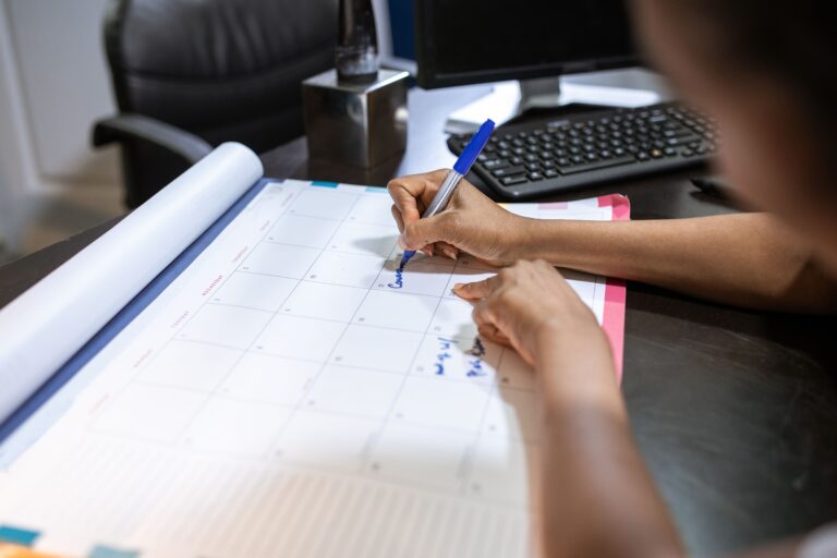 Person writing tasks into a time blocking weekly planner calendar on a desk
