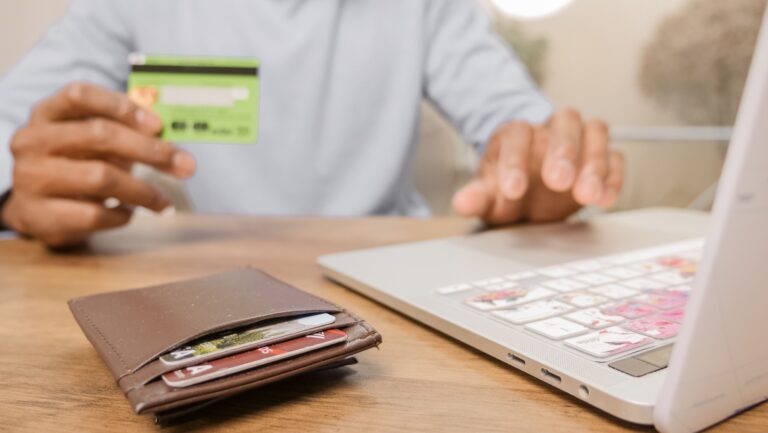 Hands holding a bank card next to a laptop while shopping online
